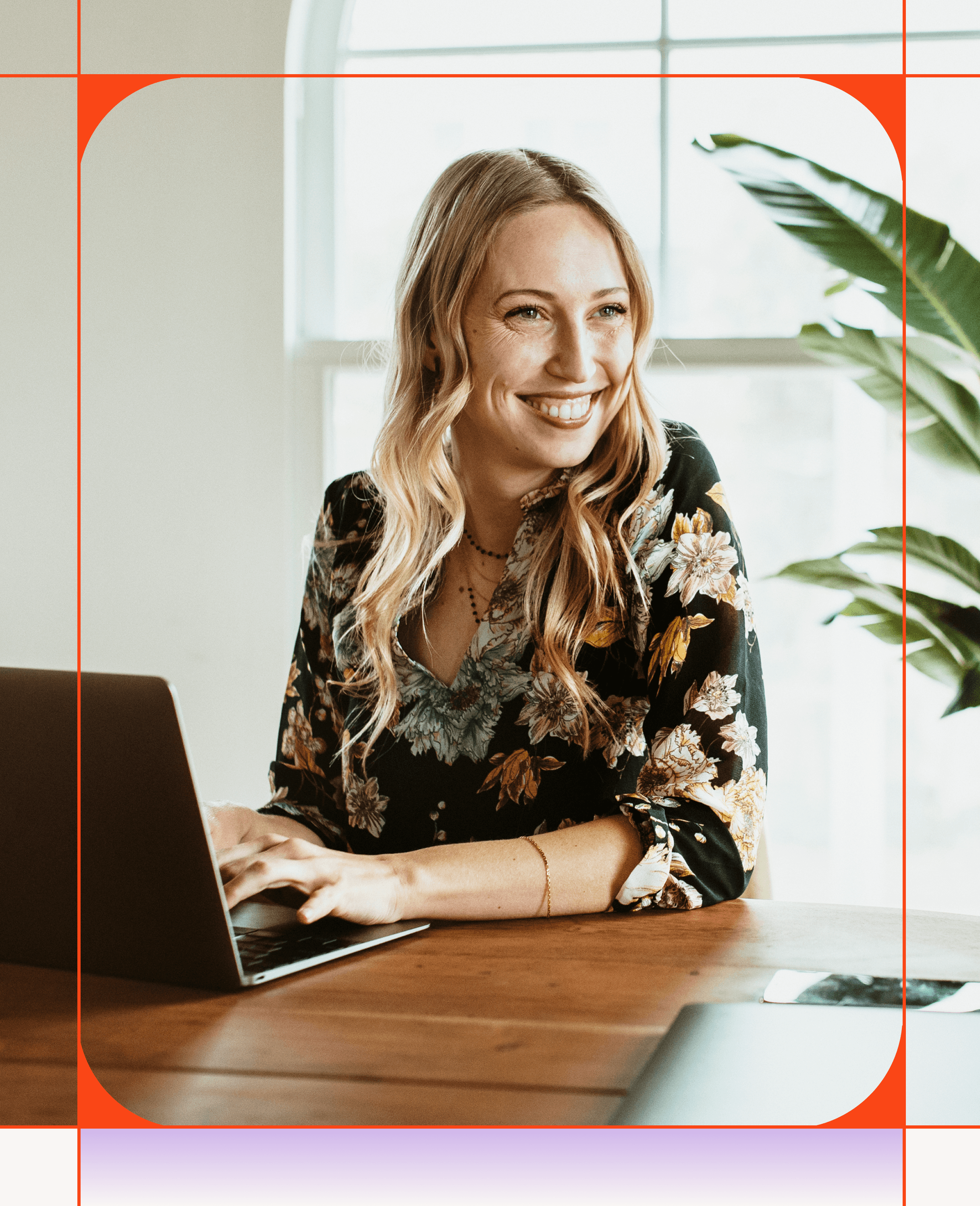 Une femme blonde souriante assise à une table en bois et tapant sur un ordinateur portable.